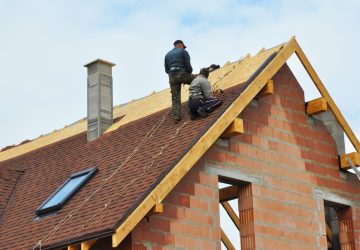 Roofing Construction and Building New Brick House with Modular Chimney, Skylights, Attic, Dormers and Eaves Exterior. Roofers Install, Repair Asphalt Shingles or Bitumen Tiles on the Rooftop Outdoor.